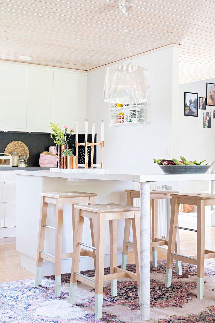 White modern breakfast bar and wooden bar stools in open-plan kitchen