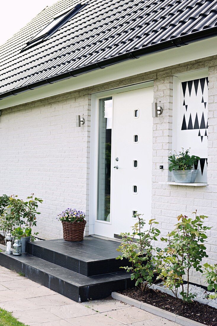 Wohnhaus mit geweisselter Ziegelfassade, vor weisser Haustür schwarze Podeststufen, seitlich schmale Beete