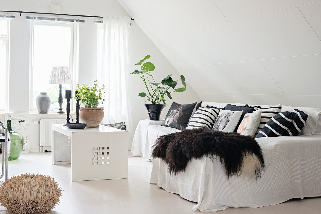 Animal-skin blanket, many scatter cushions and white throw on sofa and coffee table in lounge area in converted attic