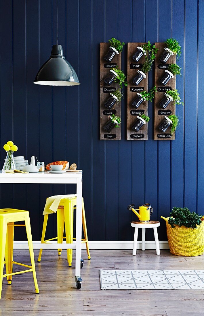 Drei Holzbretter mit angeschraubten Aufbewahrungsgläsern bepflanzt mit verschiedenen Küchenkräutern an blauer Holzpaneelwand im Essbereich aufgehängt - DIY Recycling