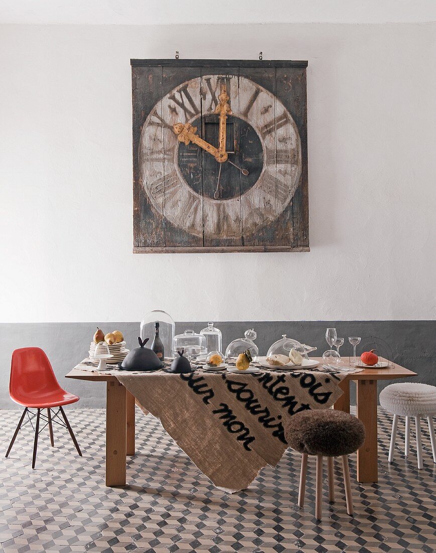 Raum im Stilmix mit Keramikfliesen, gedecktem Tisch mit Glaswaren, Eames Chair und alter Kirchturmuhr an der Wand