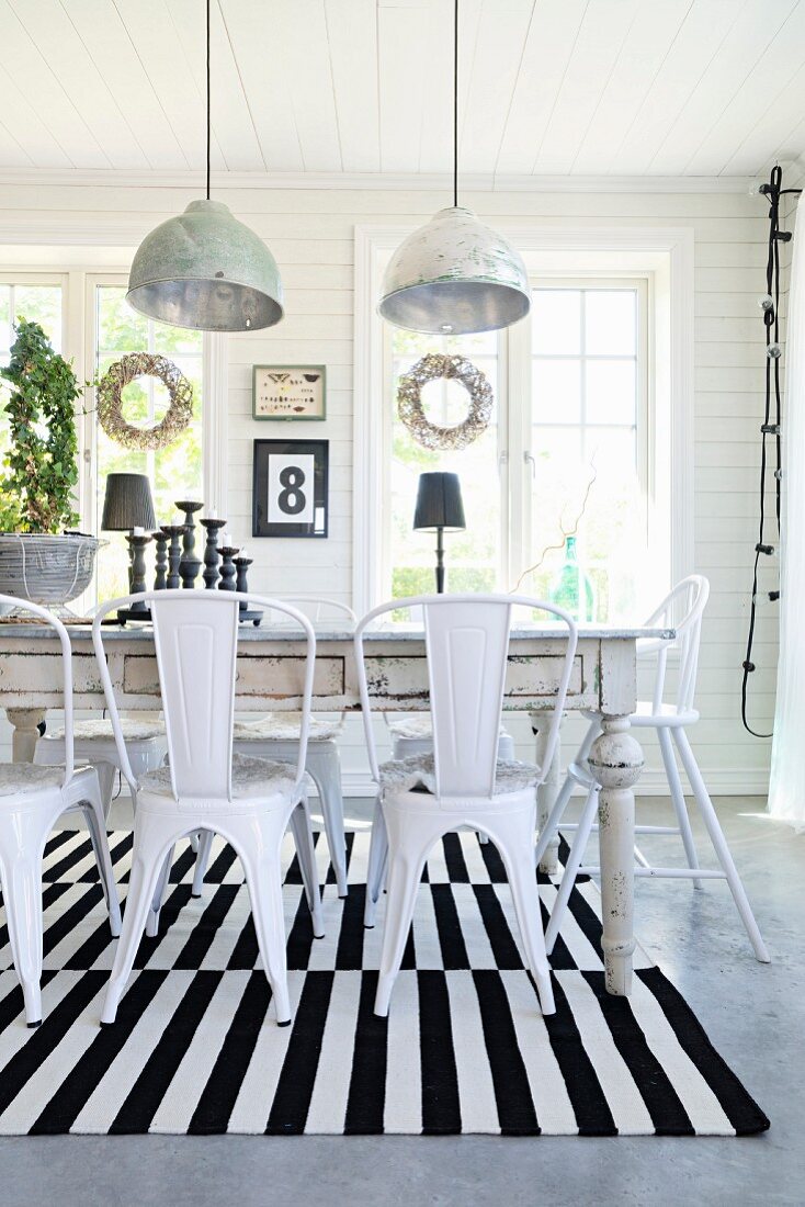 Retro metal chairs at rustic dining table on black and white striped rug below pendant lamps with metal lampshades