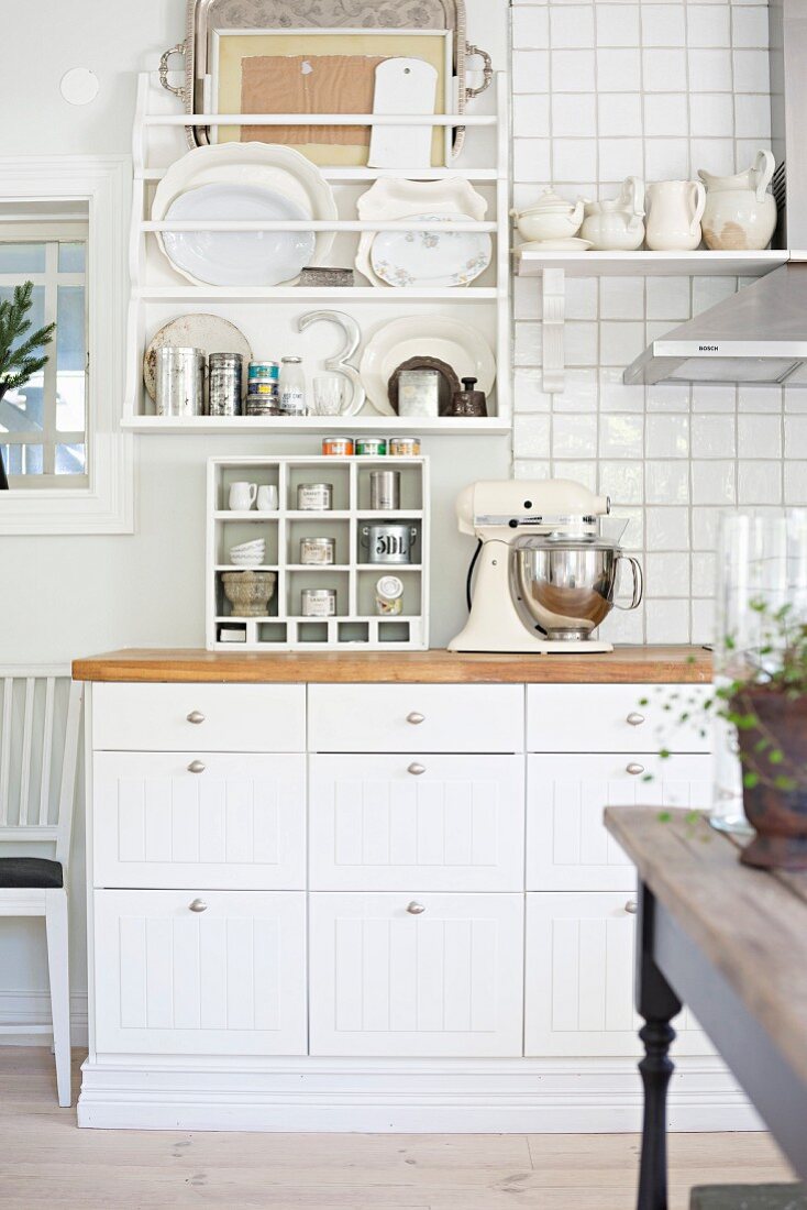 Detail of kitchen counter with white base units below plate rack on partially tiled wall
