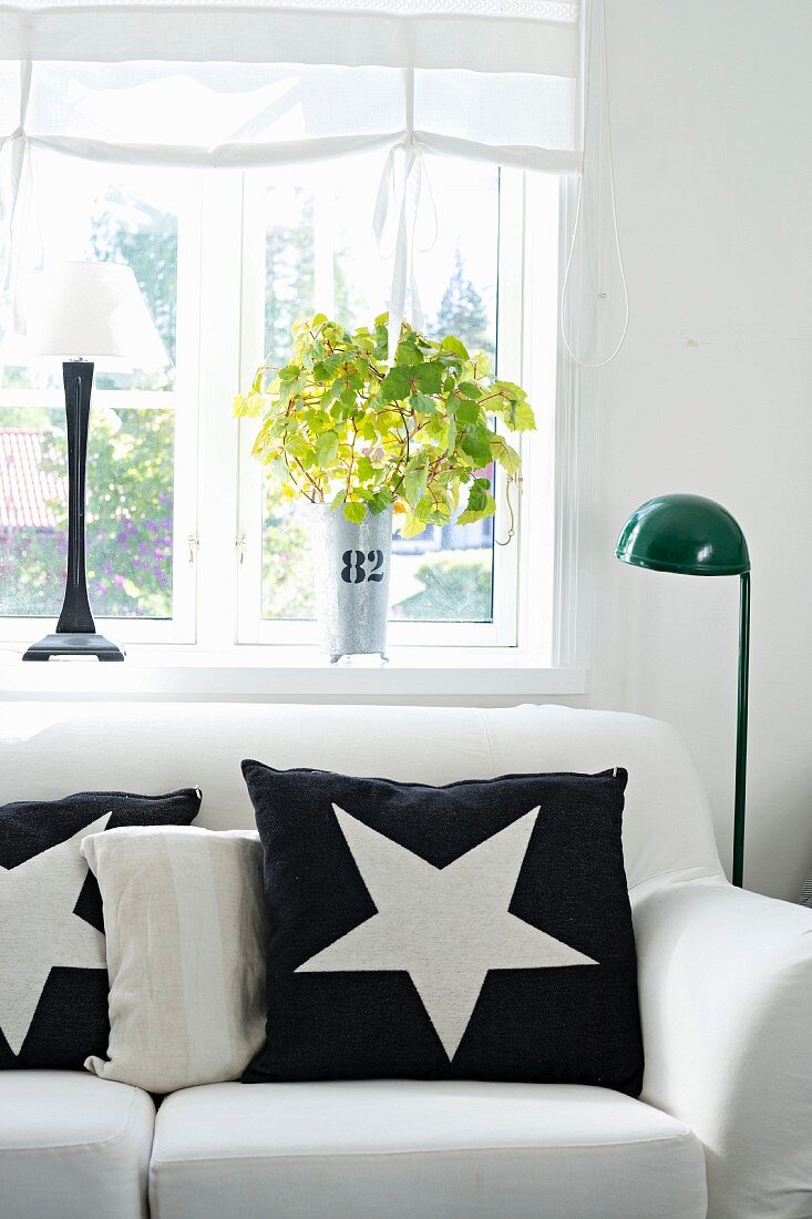 Black cushion with white star motif on white sofa next to standard lamp