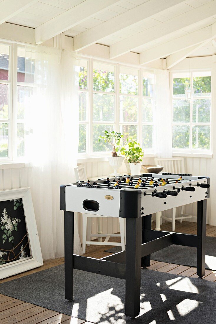 Table football table in white, wood-clad conservatory with lattice windows