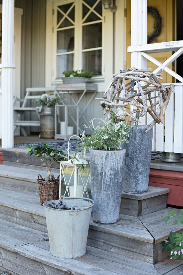 Pflanzgefässe und verzinkter Metalleimer auf Holzstufen vor Veranda