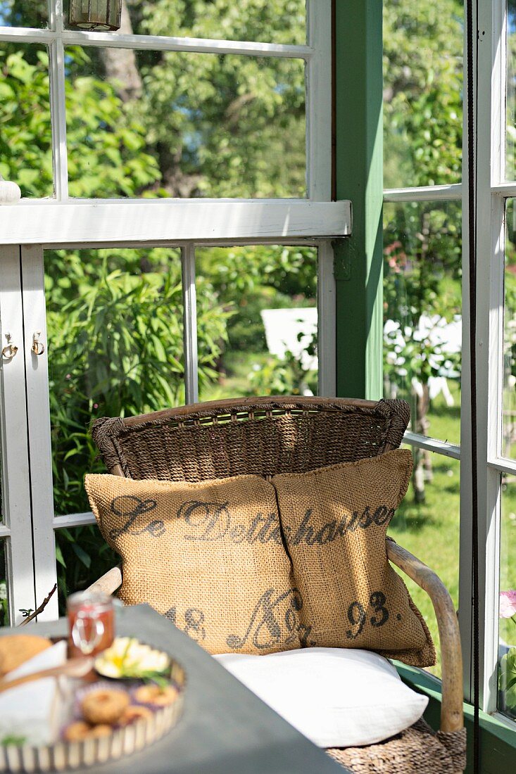Simple wicker chair with rustic cushions in corner of greenhouse