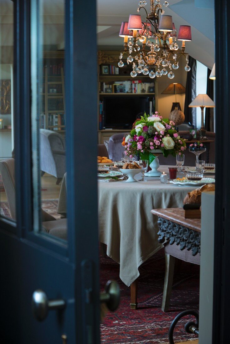 Blick durch halboffene Tür auf festlich gedeckten Tisch und eleganten Kronleuchter mit rosafarbenen Lampenschirmchen
