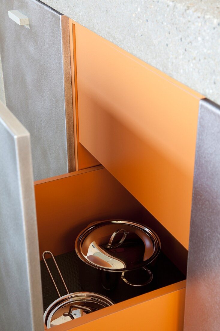 Kitchen drawer with orange interior holding stainless steel saucepans