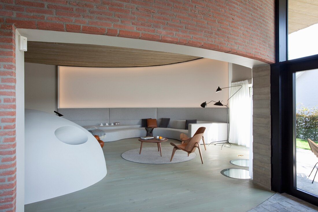 Extravagant lounge with curved wall, integrated pale grey sofa combination and custom-made, hemispherical stove