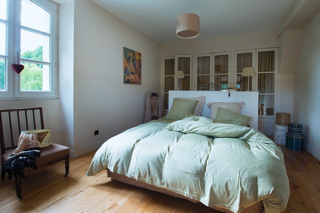 Doppelbett mit lindgrüner Bettwäsche in schlichtem Schlafzimmer, im Hintergrund Einbauschrank mit Sprossentüren