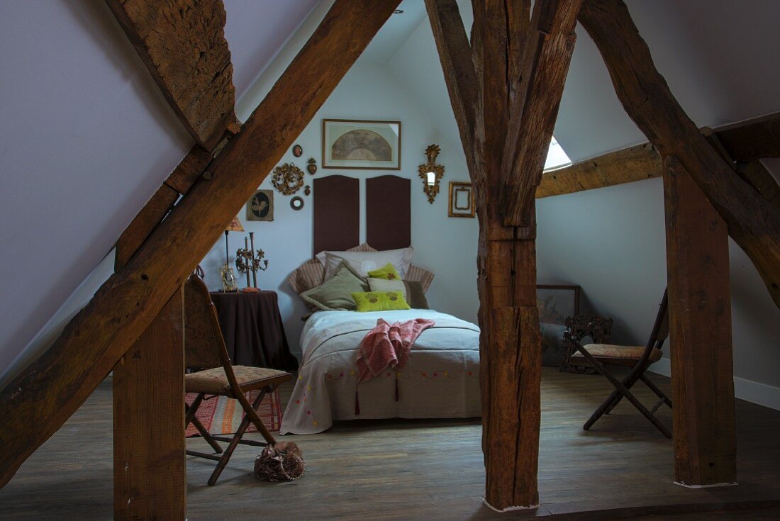Blick zwischen rustikaler Holzkonstruktion auf Bett in ausgebautem Spitzboden