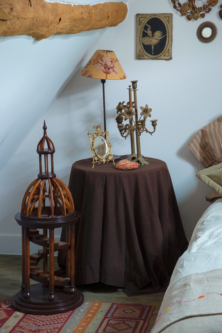 Kerzenhalter aus Messing und Vintage-Tischleuchte auf Nachttisch mit dunkelbraunem Tischdecke, davor Vintage-Architekturmodell aus Holz