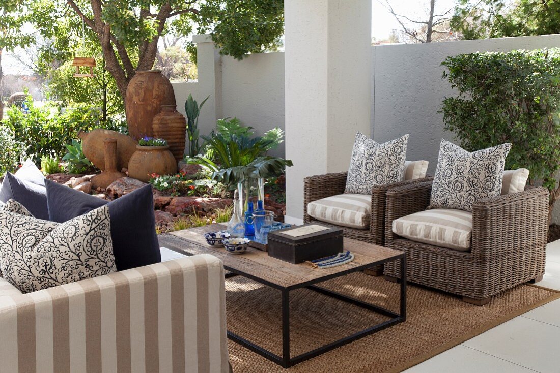 Outdoor Sitzbereich mit Couchtisch, Rattansesseln und Sofa, dekorative Tongefässe im Hintergrund