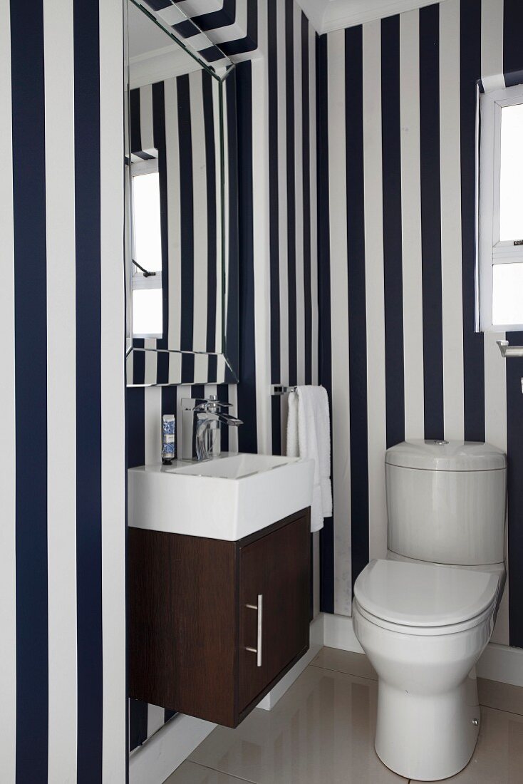 Toilet with compact washstand, bevelled mirror and blue and white striped wallpaper