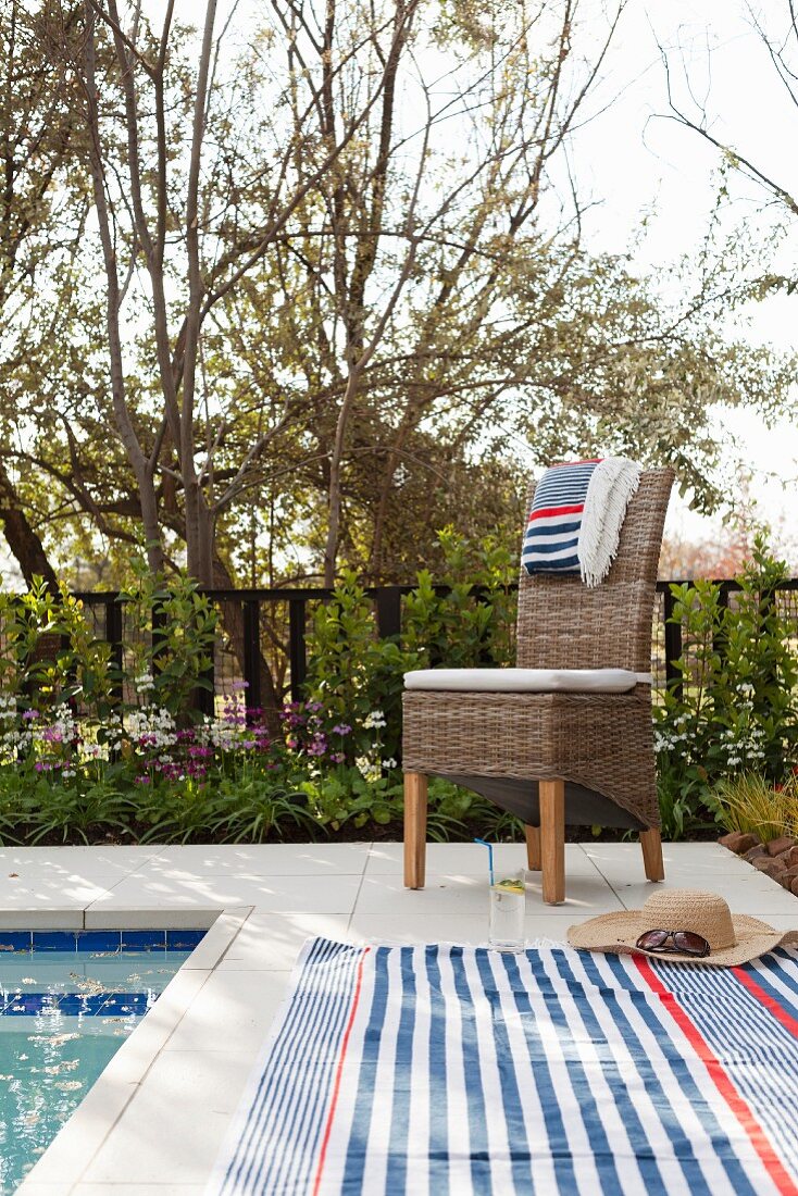 Gestreifte Handtücher auf Rattanstuhl und gefliestem Poolrand im Garten