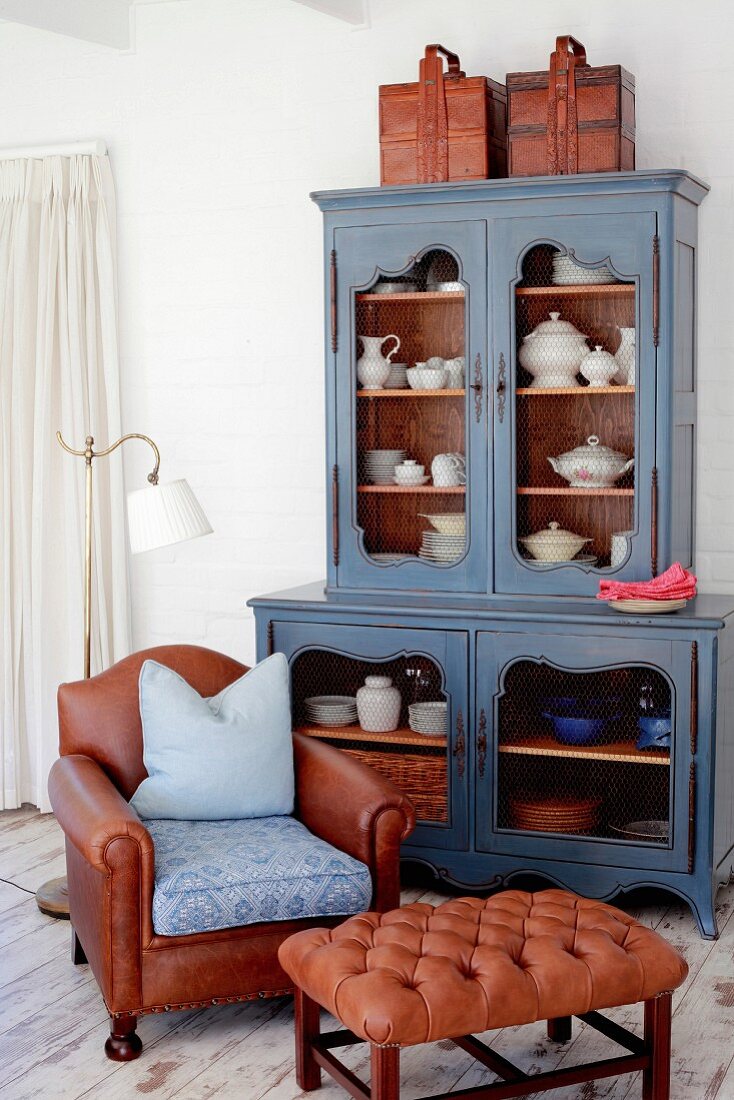 Vintage crockery in blue vintage dresser, brown leather armchair and Chesterfield footstool