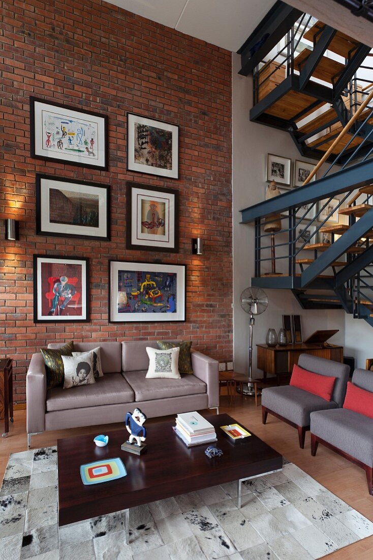 Wohnzimmer mit Bildergalerie an Backsteinwand in einem Loft mit Retromöbeln, Treppe im Industriestil