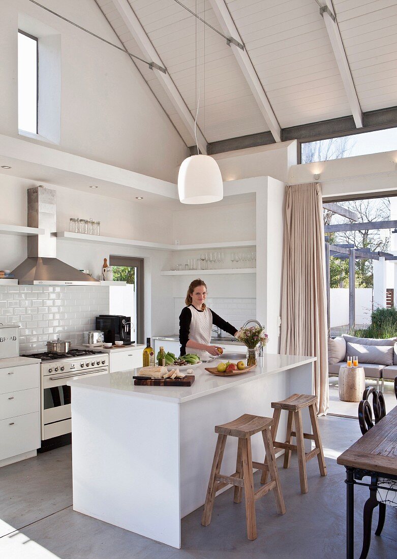 Junge Frau kocht in weißer, offener Küche mit Kücheninsel, offenem Dach und Sichtbalken