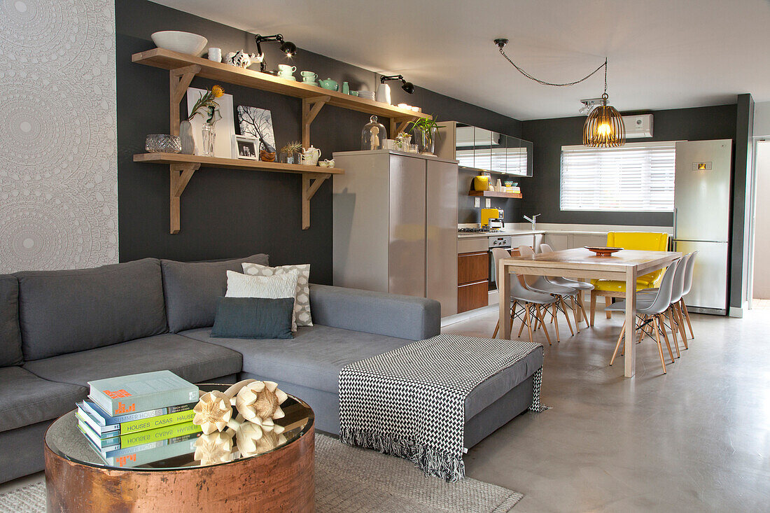 Copper coffee table with mirrored top, grey corner sofa, dining area and kitchen area with charcoal walls in open-plan interior