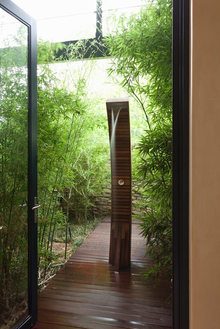 Blick auf Holzsteg mit Brunnenskulptur in Bambusgarten