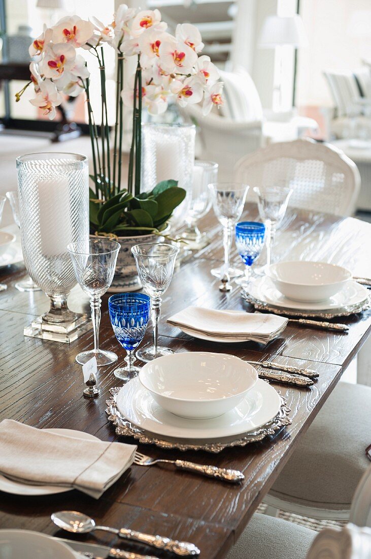 Ausschnitt aus gedecktem Tisch mit Kristallgläsern, weißem Geschirr, Silberbesteck und einer Orchidee