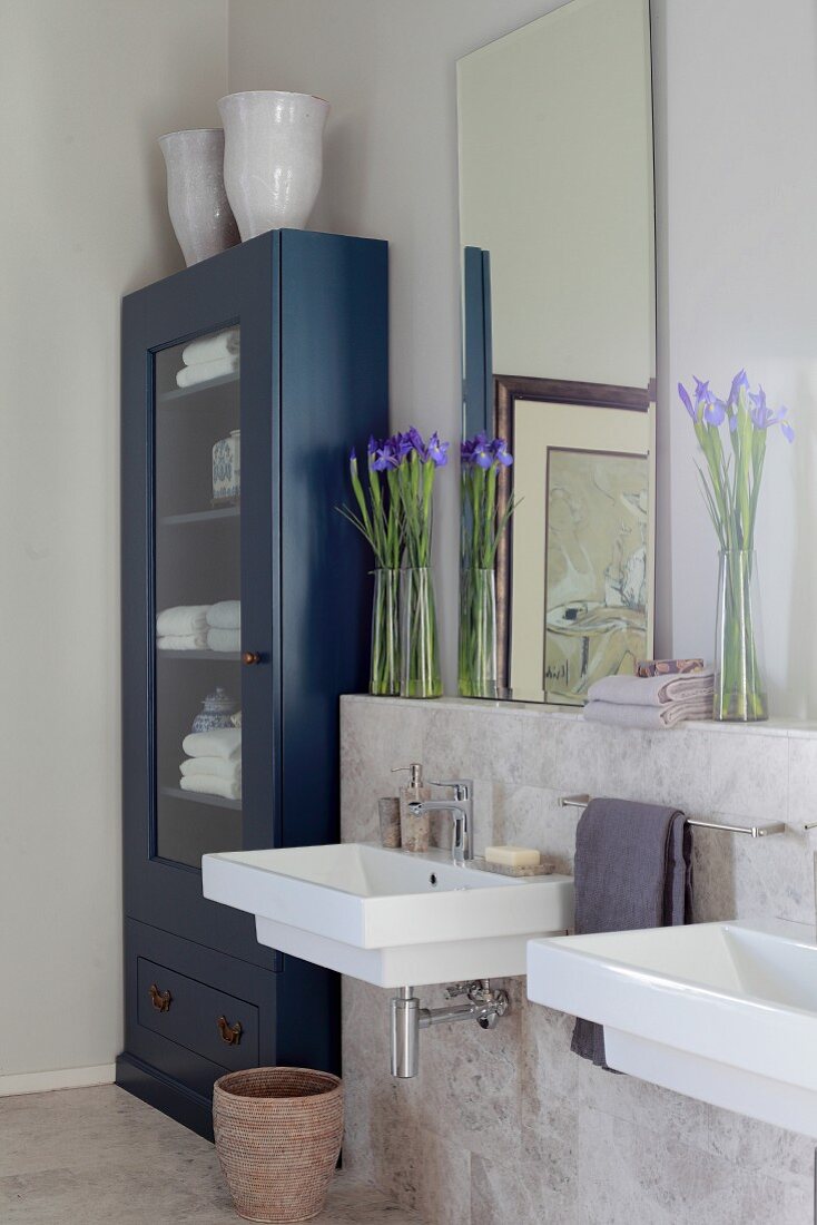 Spiegel und Irissträusse auf Sims über Waschbecken, daneben blau gestrichener Vitrinenschrank mit Handtüchern