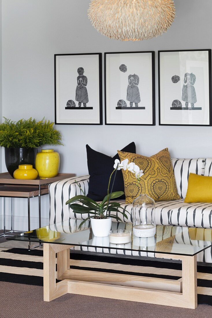 Sofa mit gestreiftem Bezug, Glastisch und gelbe Farbakzente durch Kissen und Vasen