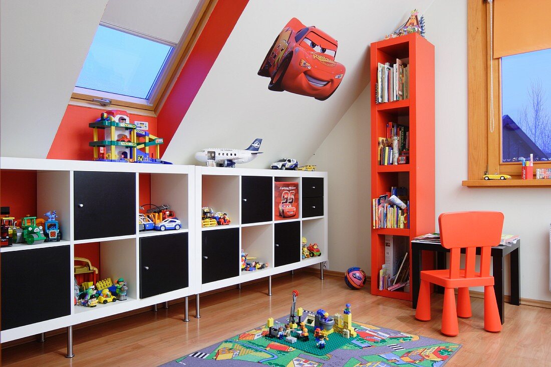 Modern sideboard with alternating open-fronted compartments and black modules, red chair and tall set of shelves in child's attic bedroom