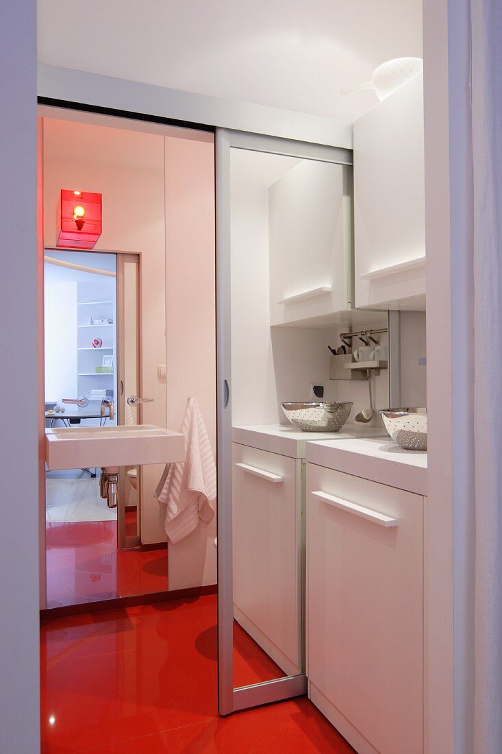 Kitchenette with open mirrored sliding door leading to bathroom with continuous orange floor