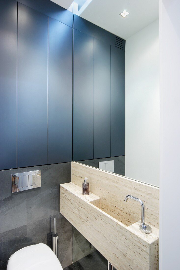 Waschtrogartiges Becken aus Stein vor vollflächigem Wandspiegel, seitlich Einbauschrank mit schwarzen Türen im Designerbad