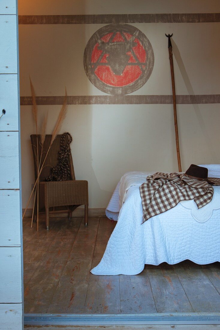 Blick von Aussen in ein Schlafzimmer auf Bett mit weisser Tagesdecke, im Hintergrund bemalte Wand