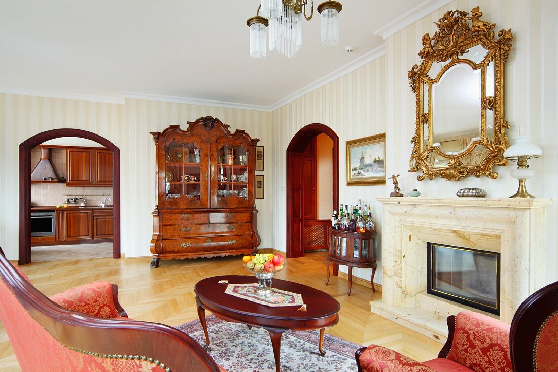 Loungebereich mit antikem Couchtisch vor offenem Kamin und Spiegel mit geschnitztem Goldrahmen an Wand, in herrschaftlichen Wohnzimmer