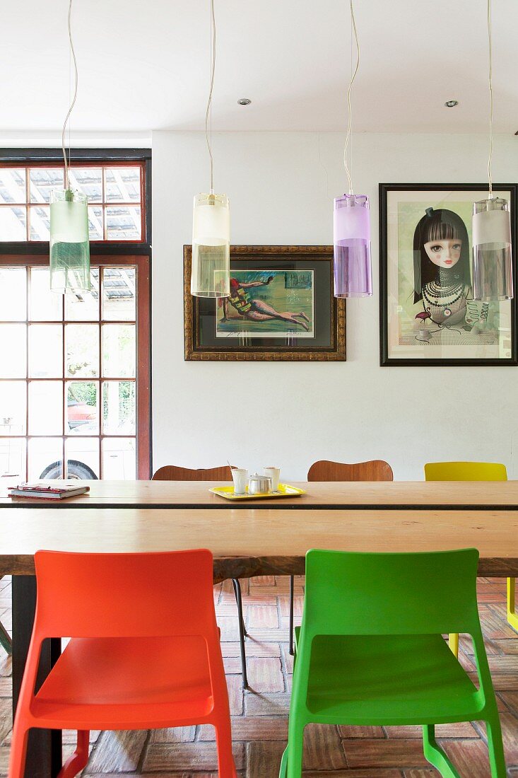 Retro Pendelleuchten über Tisch mit Baumstammplatte, vorne Kunststoffstühle, moderne Kunst im Hintergrund