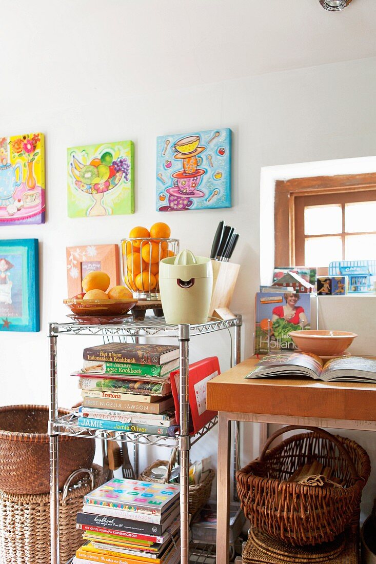Cookery books and retro citrus press on metal shelves below colourful acrylic paintings on wall