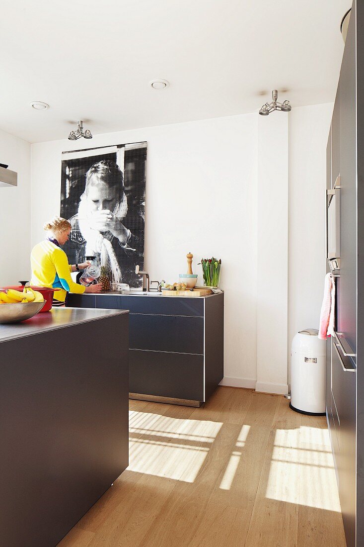 Blick in offene Küche mit Frau im Hintergrund, dunkle Unterschränke und heller Holzboden