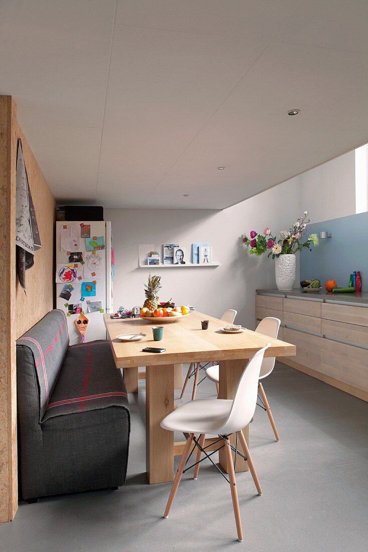 Gemütliche Wohnküche mit Holztisch, gepolsterter Sitzbank und weißen Eames Chairs