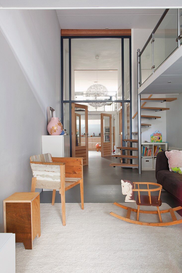 Offener moderner Wohnbereich mit Wendeltreppe zur Galerie, Retro Holzschaukelpferd und Blick durch Verglasung in hohe Diele und Küche