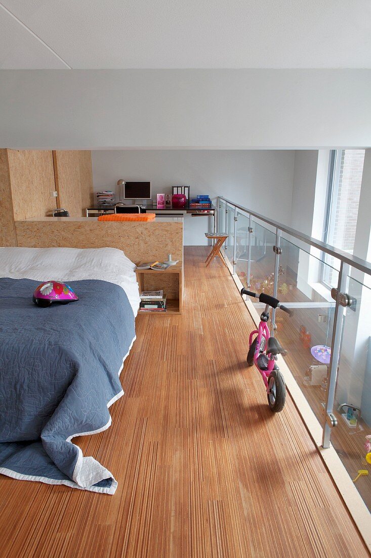 Sleeping area and study area partitioned by fitted furniture made from OSB board on gallery with glass balustrade and stainless steel handrail