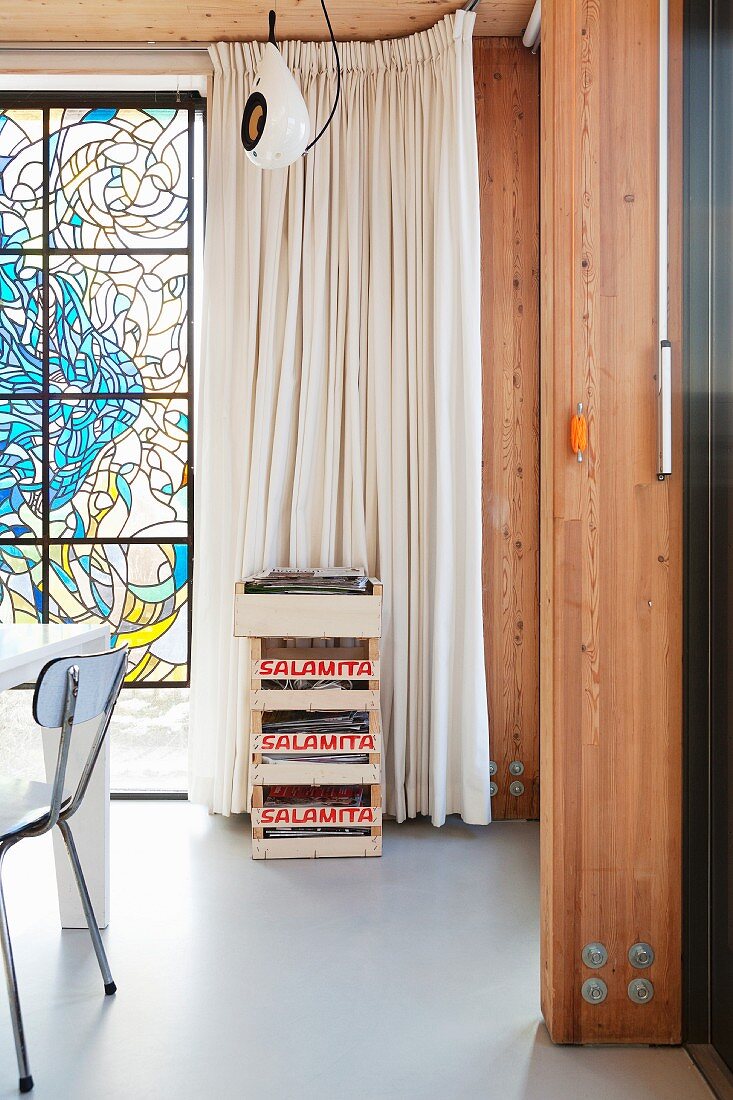 Stack of wooden crates in front of floor-length pale curtain next to stained glass window