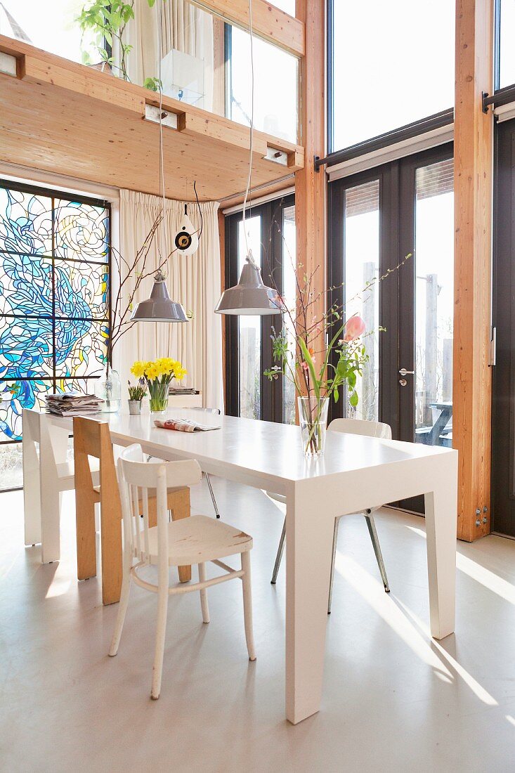 White dining table and various chair in open-plan interior below wooden gallery