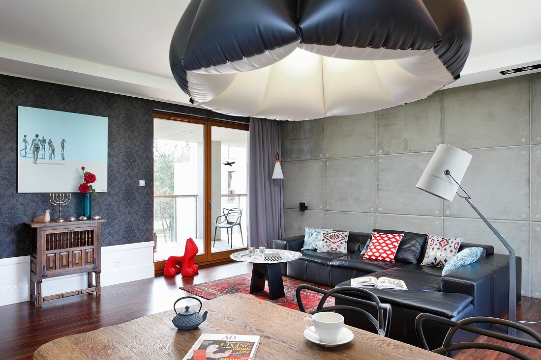 Eclectic style in open-plan interior with inflatable lampshade, black leather couch and exposed concrete wall