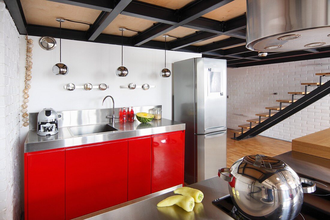 Blick auf Küchenzeile mit roten Unterschränken, seitlich Edelstahl Kühlschrankkombination in Loft-Wohnung