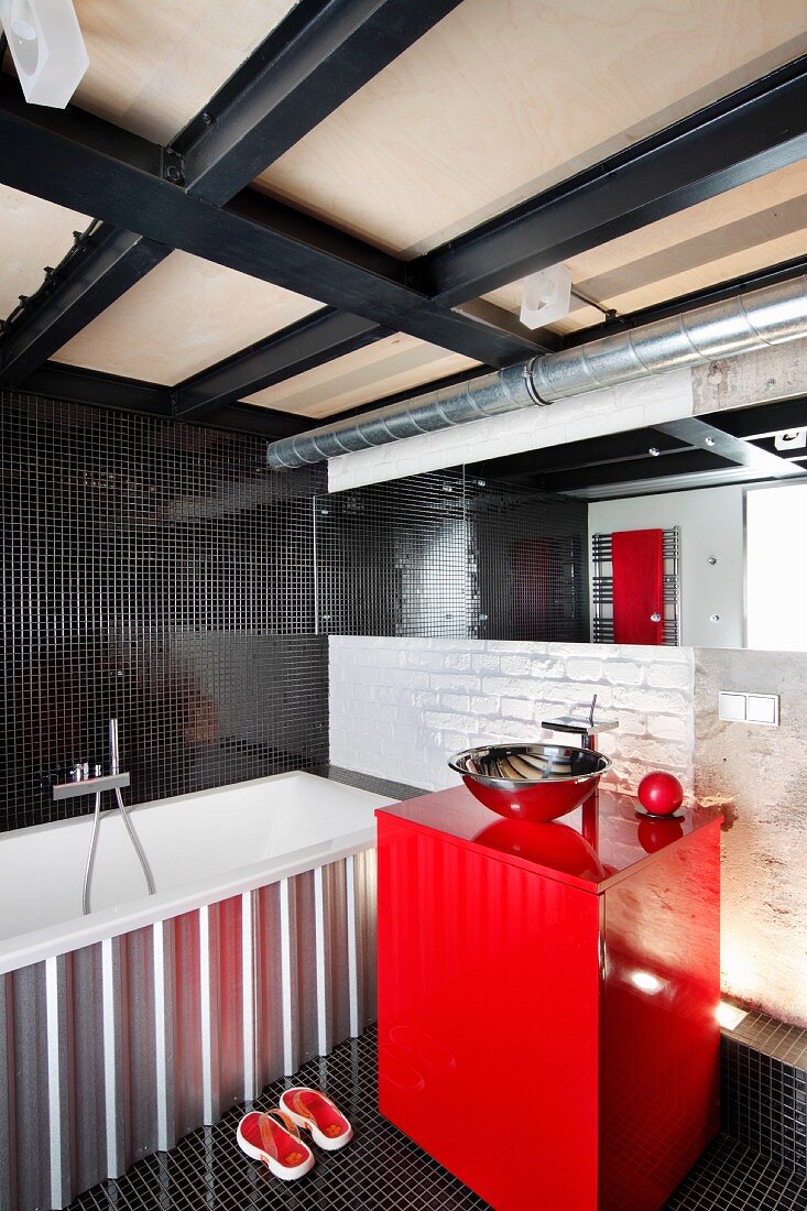 Red washstand with metal basin next to bathtub; black mosaic tiles on wall and floor