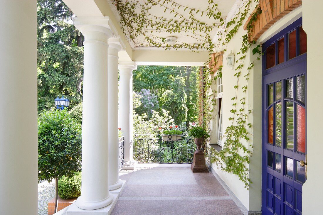 Colonial-style veranda with row of columns in summer garden outside house with blue front door