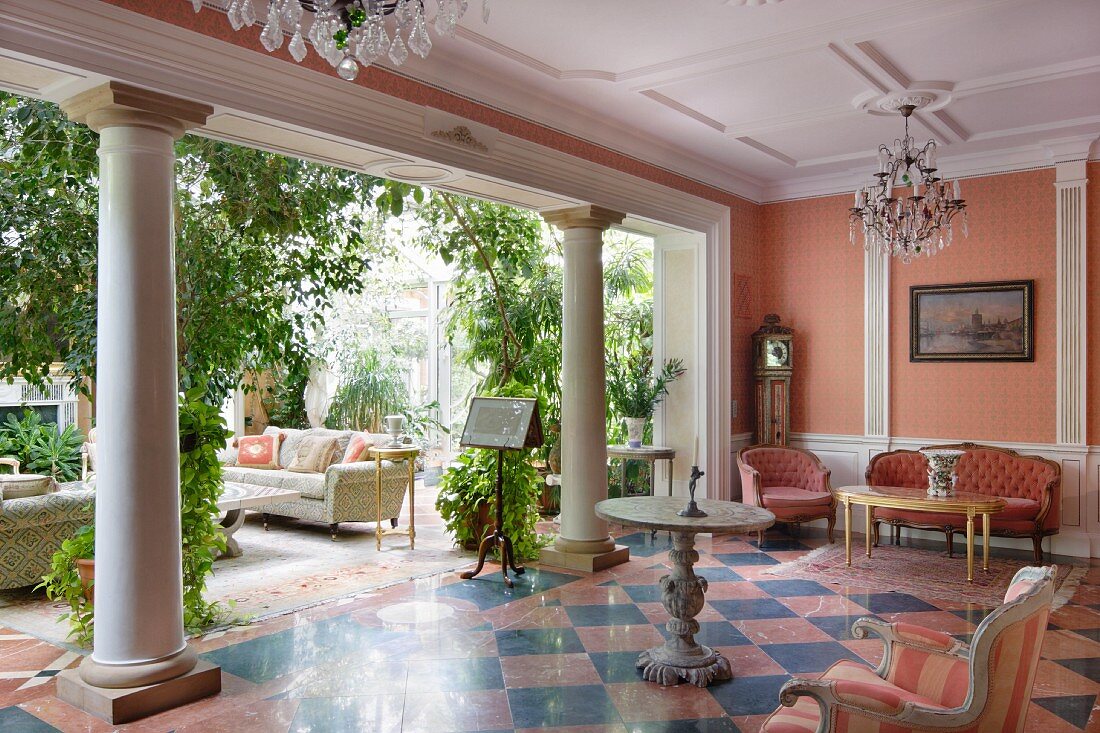 Lounge with chequered tiled floor and row of columns leading into conservatory filled with green plants