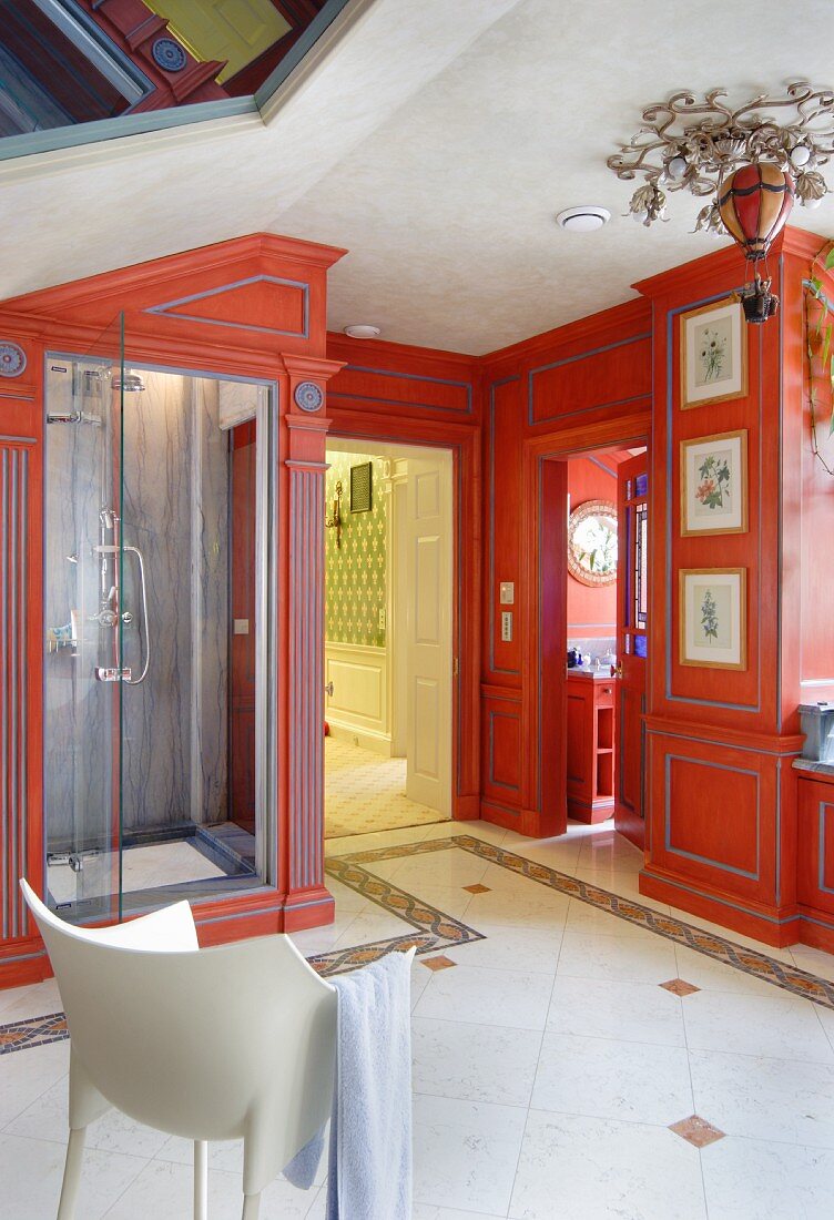 White armchair in luxurious bathroom with red-painted custom fitted cabinets and shower cubicle to one side
