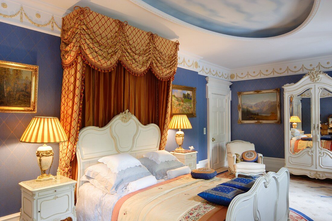 Luxuriöses Schlafzimmer im Rokoko Stil, Doppelbett mit weißem, geschwungenem Rahmen und Baldachin, seitlich Tischleuchte auf Nachtkästchen