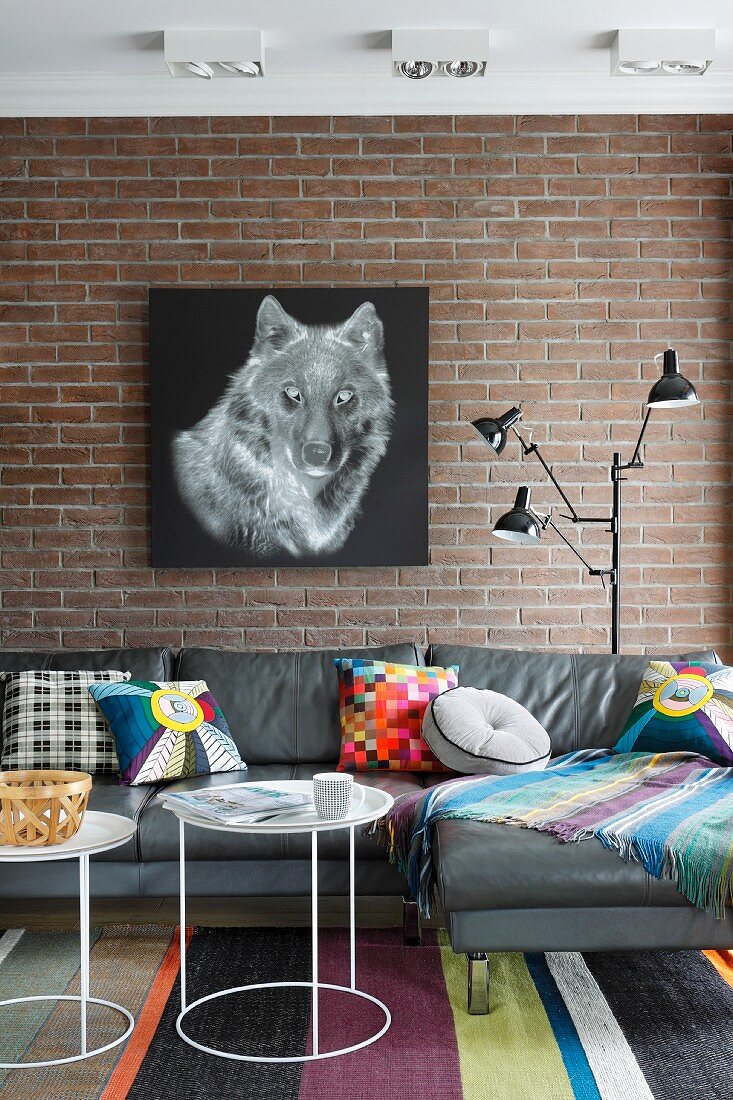 Picture of wolf on brick wall above grey leather sofa with colourful scatter cushions