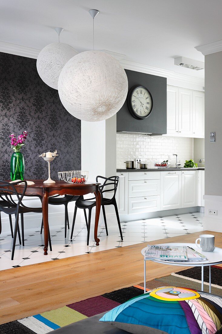 Offener Wohnraum mit weissen Ballonleuchten über Essplatz und Coffeetable, weiße Küchenzeile im Hintergrund